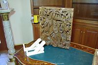 Photo showing the Asian carved wood panel with intricate human figures and a pair of marble bookends on a wooden table.