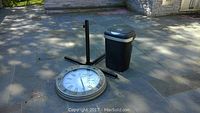 Photo of the floor clock face, umbrella stand base, and trash can on stone patio.
