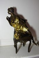 Full view of the statuette showing the woman seated sideways on the chair with one leg extended backward.