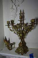 Four-prong brass candelabra with detailed scroll and floral design, showing full height and base detail.