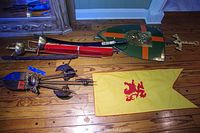Wide view of the medieval decorative weapons, shield, banner, and swords laid out on wooden floor.