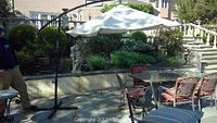 Wide view of the large hanging umbrella set up on patio over outdoor table and chairs showing full canopy and supporting frame.
