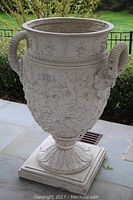 Front view of large cement urn planter showing floral relief and ram head handles.