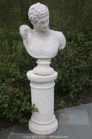 Front view of the concrete bust statue of Caesar on pedestal placed outdoors on stone patio with garden background.