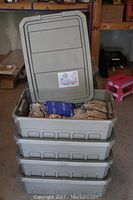 Four stacked grey plastic containers, one with lid open showing contents