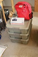 Overview of red backpack on top of three stacked olive-green containers with a white radio box in front