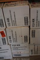 White cardboard boxes labeled '12J-RR' containing 4 jugs of Road Runner Ice Melt from Scotwood Industries, stacked on top of each other.