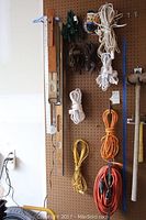 Two wooden spirit levels, multiple extension cords in various colors, and lamp cords hung on pegboard.