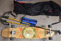 Full overview of all items - skateboard, ski poles with carrying bag, and hand grip strengthener on concrete floor