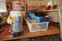 Photo of stacked rolls of tape and a basket containing blue and white label makers, pens, and other small office supplies.
