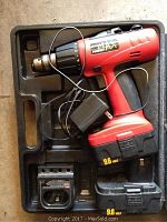 Top view of red and black cordless drill with 9.6 volt battery attached, battery charger and power cord inside molded plastic carrying case