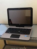 Front view of the silver HP TouchSmart laptop showing the keyboard, touchpad, and cracked touchscreen.