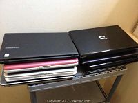 Stack of 8 various laptops on a laptop desk.