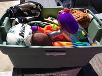 Overview of green plastic bin filled with sports balls, gloves, water guns, and other toys.