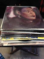 Stack of various vinyl records with a portrait of a woman on the top record cover.