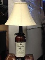 Full view of the lamp showing the large whiskey bottle base with label and beige fabric lampshade.