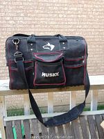 Front view of black Husky tool bag showing main compartment zipper, external pockets, and shoulder strap hanging down. Bag shows wear and dirt marks.