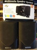 Photo showing multimedia speaker system box and two black bookshelf speakers with front grill, brand Mission visible.