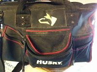 Close-up photo of the black Husky tool bag exterior with red trim and Husky logo on the front pocket.