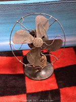 Front view of vintage GE metal desk fan showing 4 metal blades with GE center logo and protective wire cage.