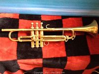 Full side view of cornet showing brass body, valves, and bell on red and black background.