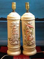 Front view of two matching vintage Asian art lamps showing detailed relief artwork of a pagoda and figures