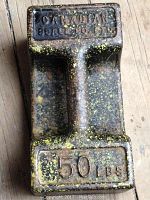Top view showing cast iron dumbbell top with 'CANADIAN SCALE CO. LTD' and '50 LBS' embossed, with yellow paint speckles and patina.