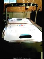 Full view of the Sportcraft Turbo air hockey table showing the white play surface with printed air hockey markings, legs, and upper frame with scoreboard and speaker system.