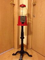 Full view of the bubble gum dispenser showing the red and glass globe top and black ornate cast iron base and stand.