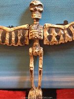 Close-up photo of the wooden skeleton figure with wings extended, showing details of skull, ribs, and wing segments.