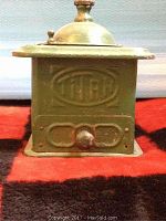 Front view of the olive green metal vintage coffee grinder showing embossed 'TITAN' logo and small drawer at base.