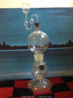 Front view of the glass measuring device showing two spherical chambers stacked vertically, with a cork on top and a glass tube with spheres.