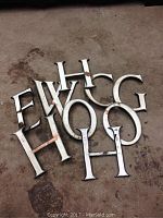 Overview photo of all 9 weathered copper letters displayed together on a floor showing letters E, W, H, H, H, C, G, O, O