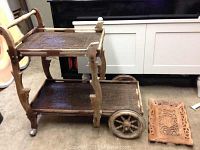 Side view of the wooden tea cart showing its structure, wheels including one large broken wheel detached from the cart, and carved wooden shelves/trays.