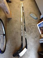 Two one-piece left handed hockey sticks side by side on the floor, one Bauer and one CCM.