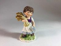 Front view of porcelain figurine showing child holding wheat and watering can on grassy base.