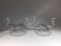 Front view of two clear glass double candlesticks showing the floral etched bases and curved arms.