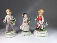 Front view of three Goebel Blumenkinder figurines showing children with flowers and toys on round white bases.