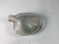 Clear glass flask shaped like a quahog clamshell, lying on its side showing ribbed texture and neck opening with no cap