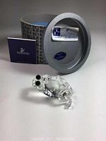 Photo showing Swarovski frog figurine, original patterned box, certificate booklet, and authenticity sticker on the box lid.