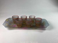 Set of six French cordial glasses arranged on decorative rectangular tray with soft floral pastel patterning, photographed from front angle