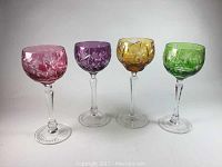 Four Bohemian cut crystal wine glasses in pink, amethyst, amber, and green colors, clear stems.