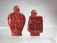 Front view of two cinnabar snuff bottles showing detailed carved landscapes and figures. Rounded bottle on left, square bottle on right.