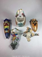 Five assorted Japanese wall pocket flower vases displayed from above featuring varied shapes and decorations including birds, a boy, and onion design.