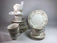 Full display of the dessert set showing stacked plates, stacked footed cups with some tissue inserted to protect them, and arranged cups on saucers.