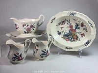 Overall view of all ceramic pieces including gravy boat on underplate, oval serving bowl, and two footed creamers with floral and bird designs