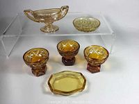 Set of seven amber glass salt cellars in various shapes and sizes displayed on a clear acrylic riser.