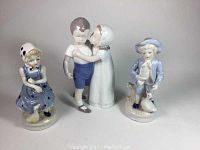 Photo showing all three figurines together: girl in blue dress, Bing and Grondahl 'Love Refused' figurine with girl kissing boy, and boy in blue vintage outfit with dog