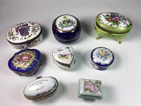 Top-down view of all 8 porcelain trinket boxes showing various shapes and hand-painted floral and heraldic motifs.
