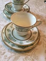 Photo showing stacked footed teacups, saucers, and dessert plates with detailed Henley floral pattern and gold edging